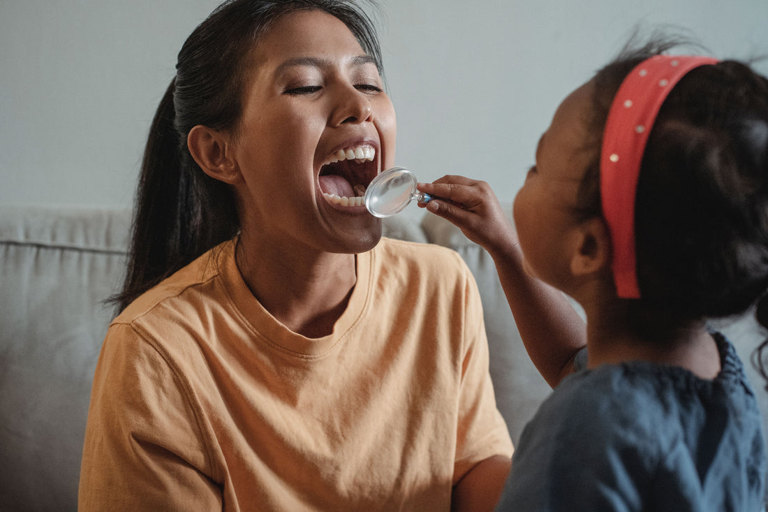 Woman opening her mouth wide while a young girl looks inside with a magnifying glass