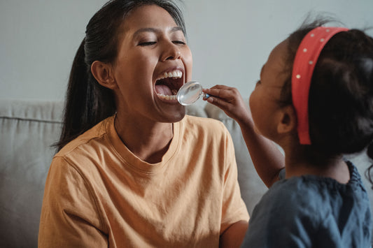 Woman opening her mouth wide while a young girl looks inside with a magnifying glass